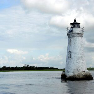 Historic white lighthouse stands against a vast ocean backdrop, under a cloudy sky.